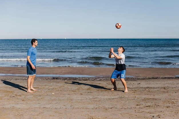 Zijaanzicht van vrienden die voetbal spelen bij het strand