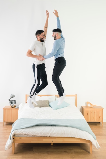 Zijaanzicht van vrolijk paar genieten van springen op bed in de slaapkamer