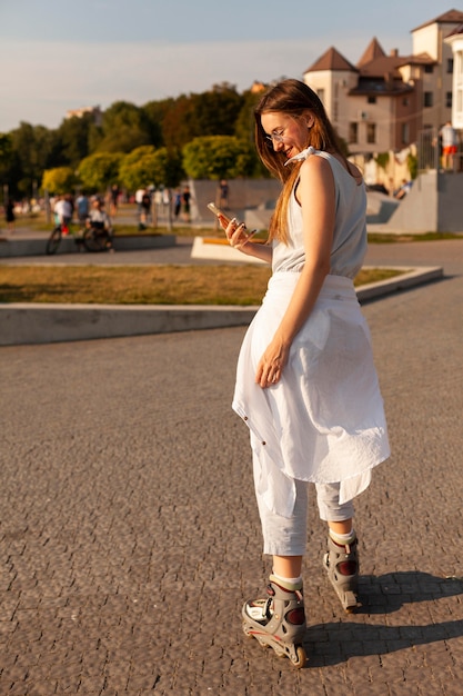 Gratis foto zijaanzicht van vrouw buitenshuis met smartphone met rolschaatsen