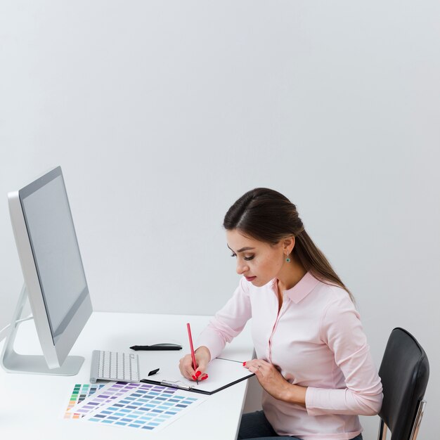 Zijaanzicht van vrouw die iets neerschrijven terwijl bij bureau