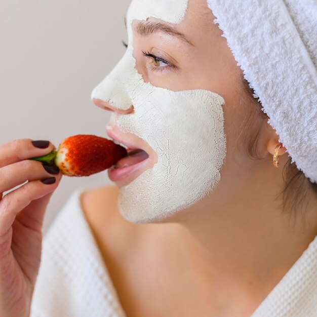 Zijaanzicht van vrouw die met gezichtsmasker aardbei eet