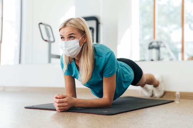 Zijaanzicht van vrouw die tijdens pandemie bij de gymnastiek met medisch masker uitoefent