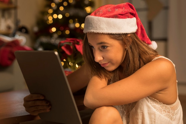 Gratis foto zijaanzicht van vrouw met kerstmuts en tablet op kerstmis