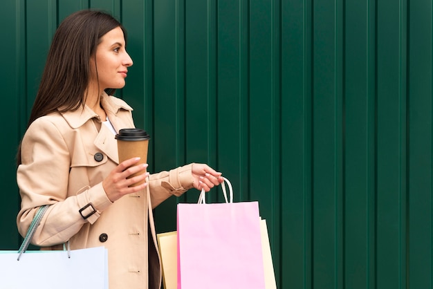 Gratis foto zijaanzicht van vrouw met koffiekopje en boodschappentassen