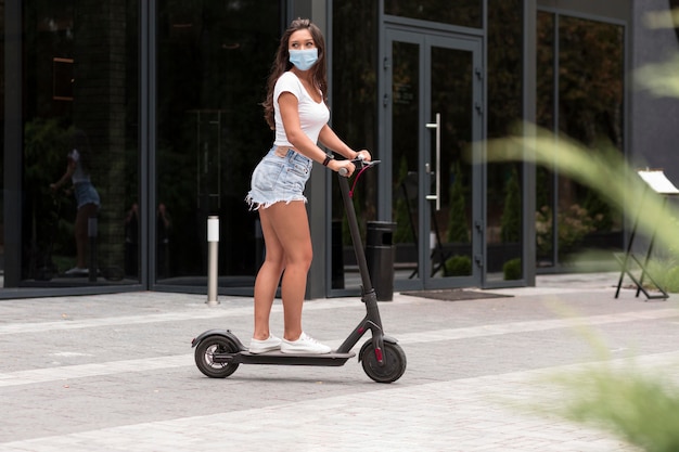 Zijaanzicht van vrouw met masker rijden op een elektrische scooter