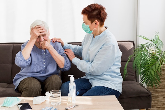 Zijaanzicht van vrouw met medisch masker die een oudere vrouw thuis behandelen