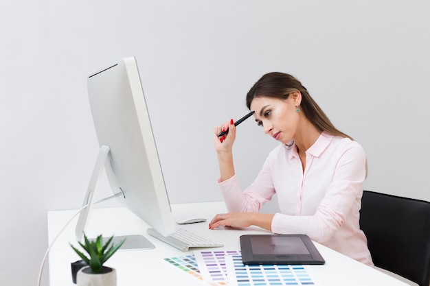 Gratis foto zijaanzicht van vrouw op het werk die en computer denken bekijken