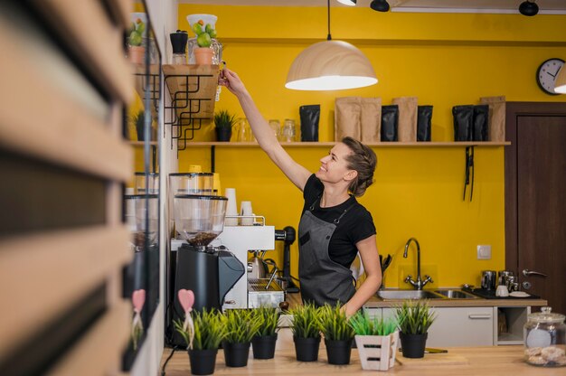 Zijaanzicht van vrouwelijke barista die in koffiewinkel werkt