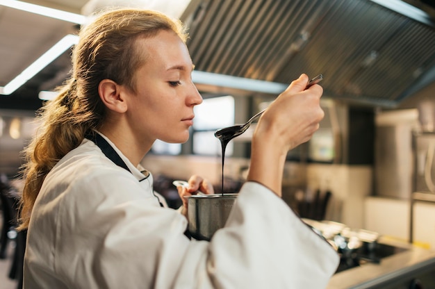 Gratis foto zijaanzicht van vrouwelijke chef-kok die saus probeert