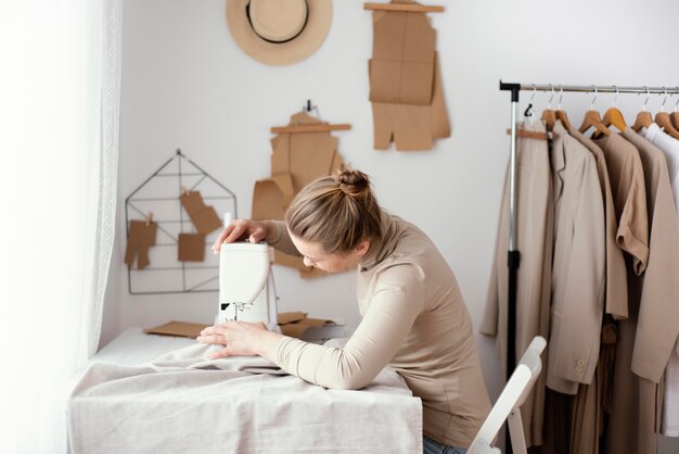 Zijaanzicht van vrouwelijke kleermaker die in de studio met naaimachine werkt