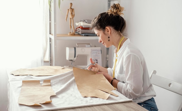 Gratis foto zijaanzicht van vrouwelijke kleermaker die in de studio werkt