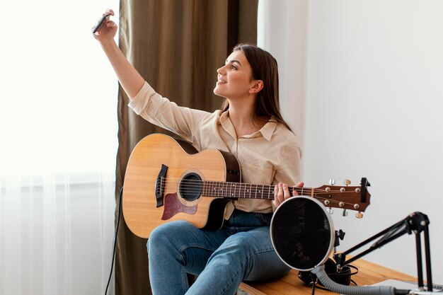 Zijaanzicht van vrouwelijke muzikant thuis selfie te nemen terwijl akoestische gitaar vasthoudt