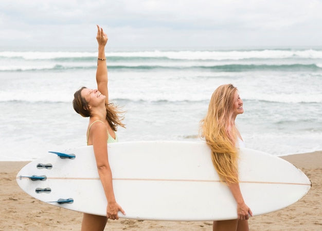 Zijaanzicht van vrouwelijke vrienden die een surfplank houden op het strand