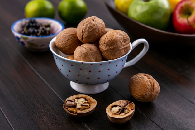 Zijaanzicht van walnoten in een kopje met appels limoen en zwarte bessen op een houten oppervlak