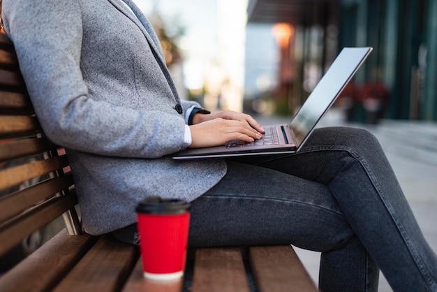 Gratis foto zijaanzicht van zakenvrouw die op laptop buitenshuis met kopje koffie werkt