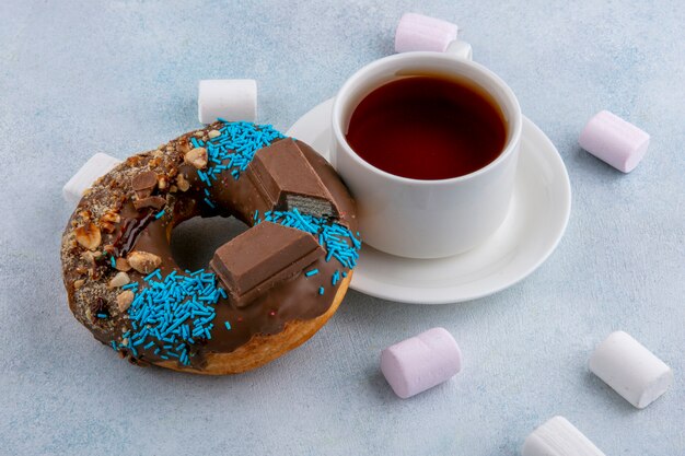 Zijaanzicht van zoete donut met marshmallows en een kopje thee op een grijze ondergrond