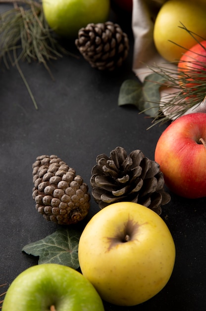 Zijaanzicht veelkleurige appels in een jute zak met dennenappels op een zwarte tafel