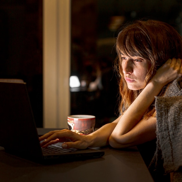 Zijaanzicht vermoeide vrouw met laptop binnenshuis