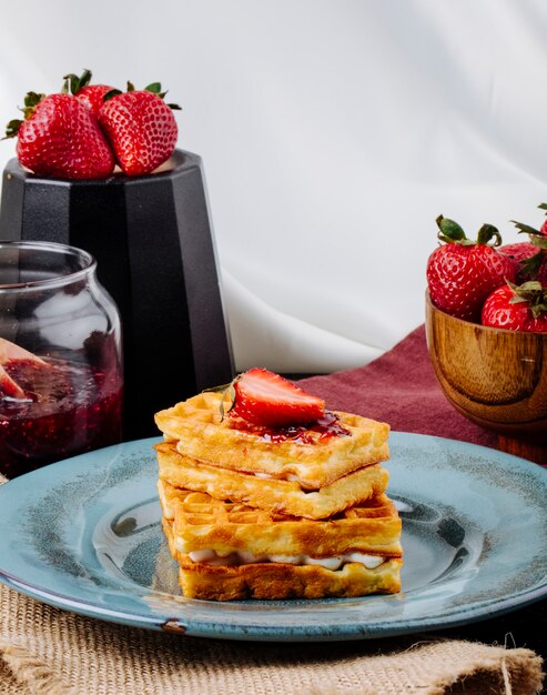 Zijaanzicht wafels met vanille crème aardbei en jam op tafel