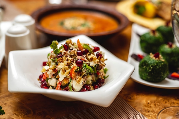 Gratis foto zijaanzicht walnoot salade met granaatappel paprika mayo greens vlees en sla op een bord