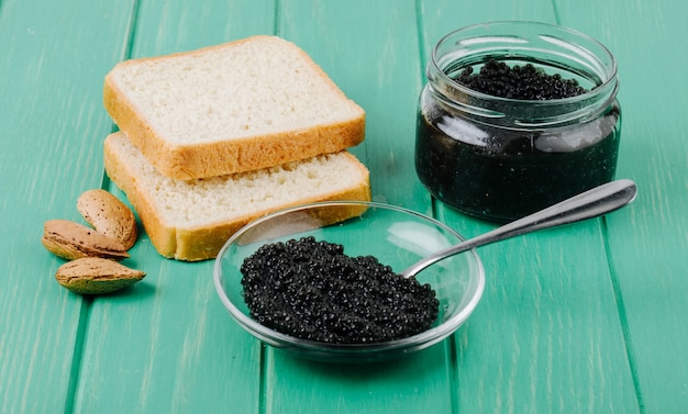 Zijaanzicht zwarte kaviaar met lepel wit brood en amandel op turquoise houten oppervlak