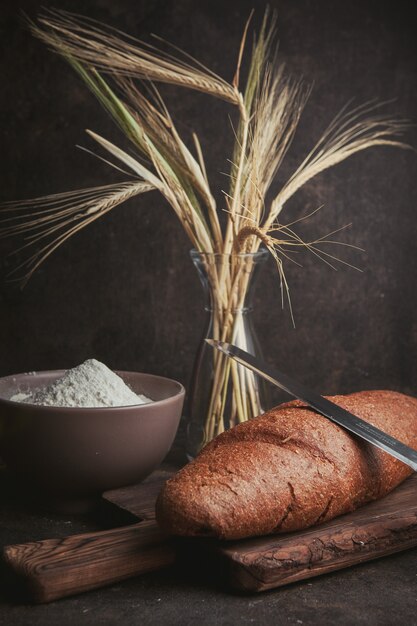 Zijaanzichtbloem in kom met tarwe, mes en brood op donkerbruin. verticaal