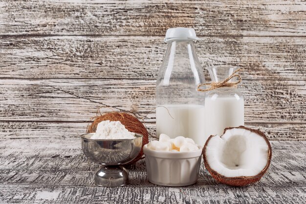 Zijaanzichtflessen melk met verdeeld in halve kokosnoten, kaas en bloem op grijze houten achtergrond. horizontaal