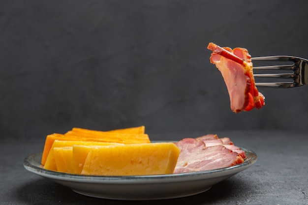 Zijaanzichthand die een voedsel met vork van een blauw bord met heerlijke snacks op een zwarte achtergrond neemt