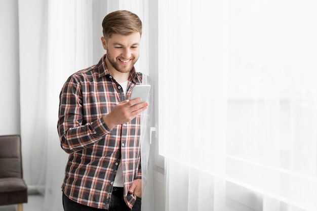 Zijaanzichtmens bij venster met mobiel