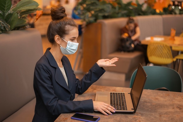 Zijaanzichtonderneemster met medisch masker dat aan haar laptop werkt