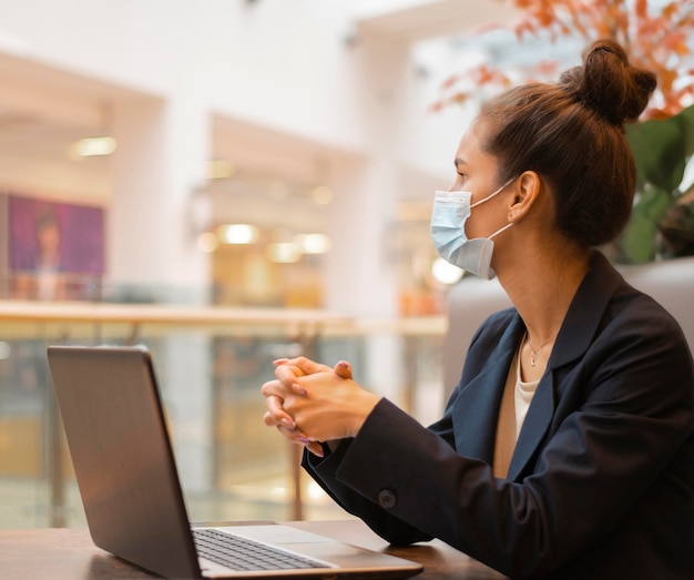 Zijaanzichtonderneemster met medisch masker dat aan haar laptop werkt