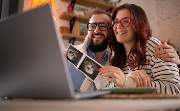 Zijaanzichtpaar dat zwangerschap met laptop aankondigt