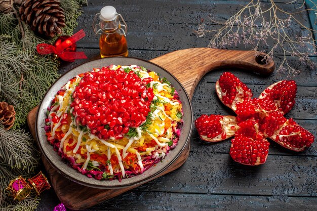 Zijaanzichtplaat van kerstvoedsel Kerstschotel met granaatappel op de snijplank gepilde granaatappelfles olie en vuren takken met kerstboomspeelgoed