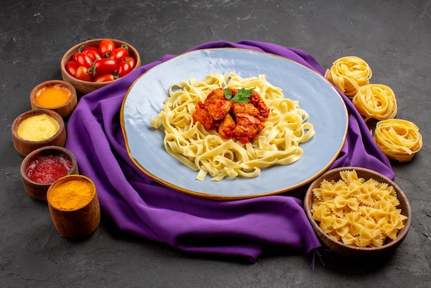 Zijaanzichtplaat van pastakommen met tomaten, vier soorten sauzen en bord pastavlees en jus op het paarse tafelkleed