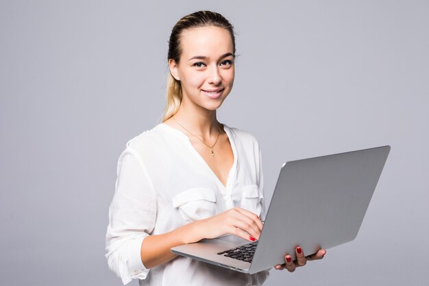 Zijaanzichtportret van een vrolijke jonge vrouw die op laptop typt die op een grijze muur wordt geïsoleerd