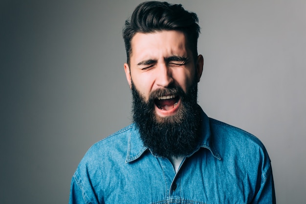 Zijaanzichtportret van schreeuwende bebaarde man - grijze muur