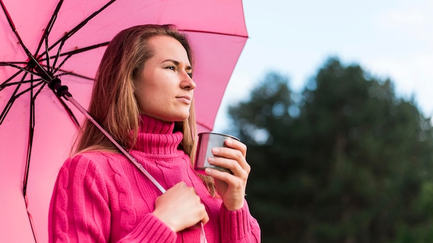 Zijaanzichtvrouw die een roze paraplu houdt