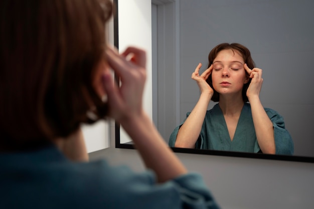 Gratis foto zijaanzichtvrouw die gezicht in spiegel masseren