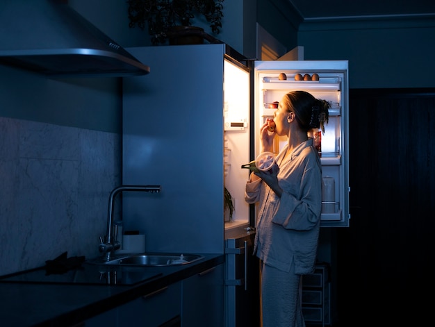 Gratis foto zijaanzichtvrouw die in de koelkast kijkt