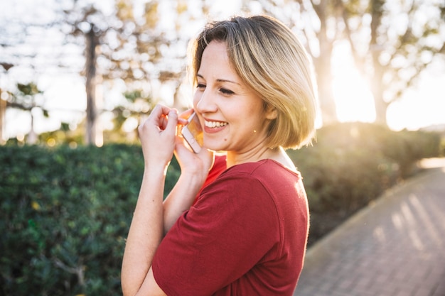 Zijaanzichtvrouw die op telefoon op parksteeg spreken