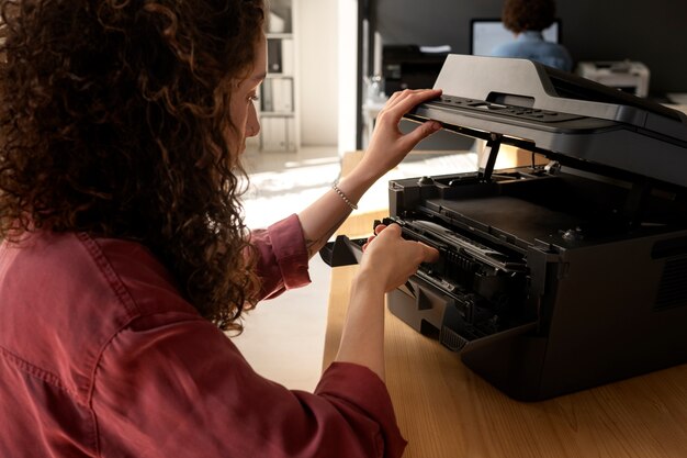 Zijaanzichtvrouw die printer op het werk gebruikt