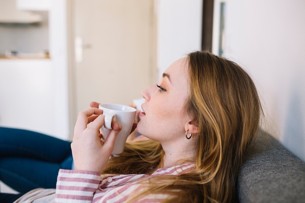 Zijaanzichtvrouw het drinken op bank