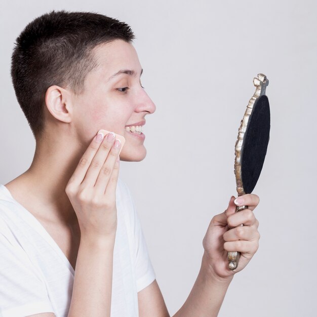 Zijdelings vrouw die haar gezicht schoonmaakt terwijl het kijken in de spiegel