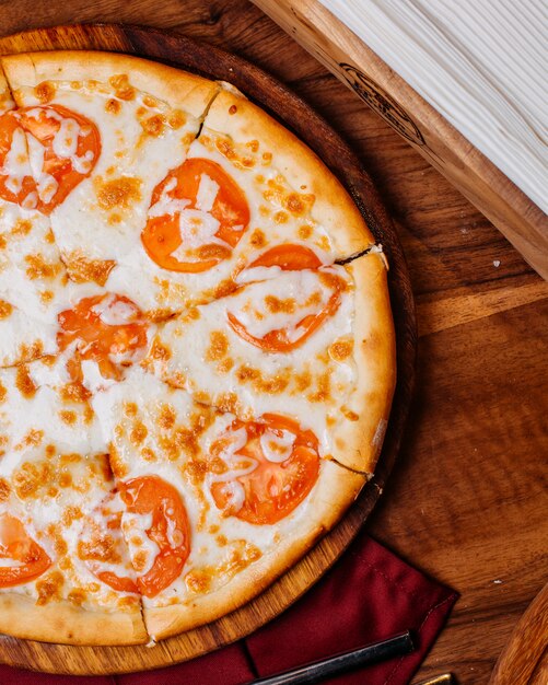 Zijkant van een pizza met tomaten en kaas op een rond houten bord