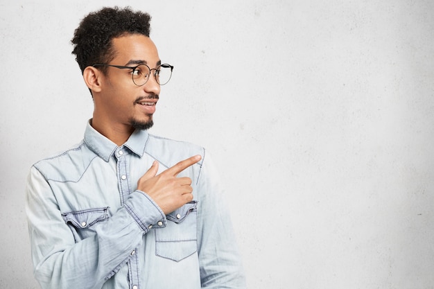 Zijwaarts portret van intelligente slimme jongeman met snor, baard en afro-kapsel, blikken met verbazing opzij