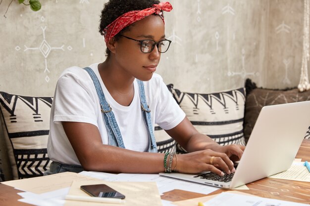 Zijwaarts schot van donkere huidskleurige werkneemster heeft zaken online, toetsenborden op laptopcomputer