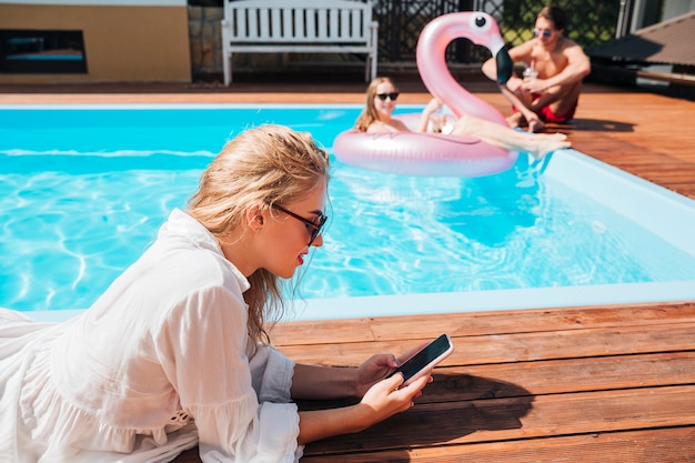 Zijwaarts vrouw die haar telefoon controleert bij de pool