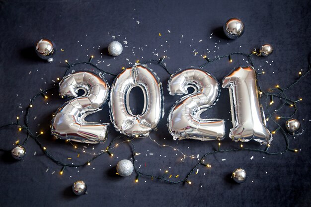 Zilverfolie ballonnen gemaakt nieuwjaarsnummer op zwarte achtergrond met garland en ballen.