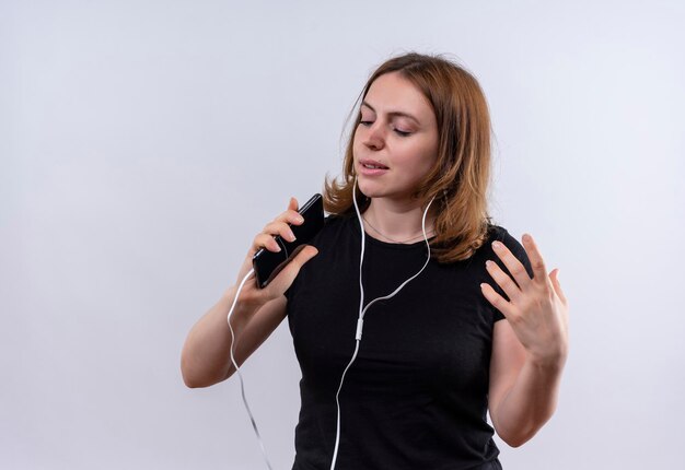 Zingende casual jongedame hoofdtelefoon dragen en mobiele telefoon gebruiken als microfoon op geïsoleerde witte ruimte met kopie ruimte