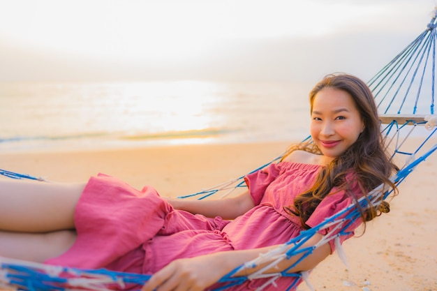 Zitting van de portret de mooie jonge aziatische vrouw op de hangmat met het strandoverzees en oce van glimlach gelukkige neary